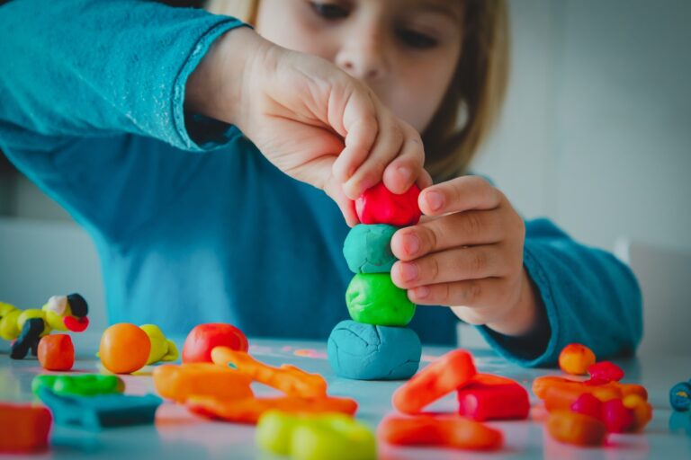 Child playing with various colors of play dough. Stacking balls of dough.