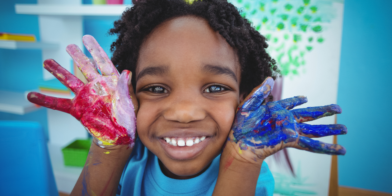 a child smiling with paint on their hands