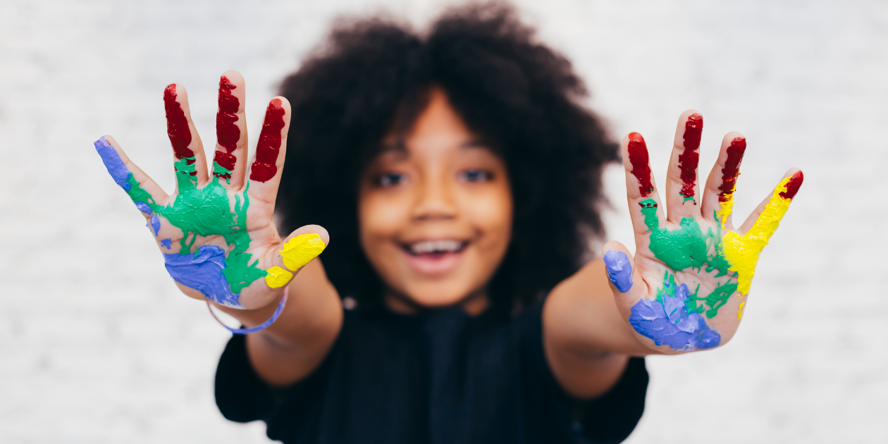 a young girl with her hands covered in paint, and smiling