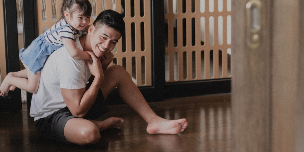 Child hanging on their father's back, while he sits on the floor. Making Your Home Autism-Friendly for Your Child