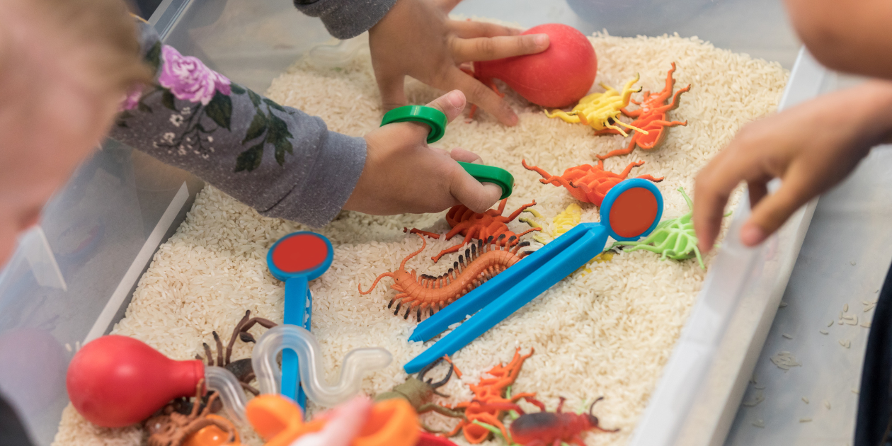 children hands playing in a box with different toys and textures