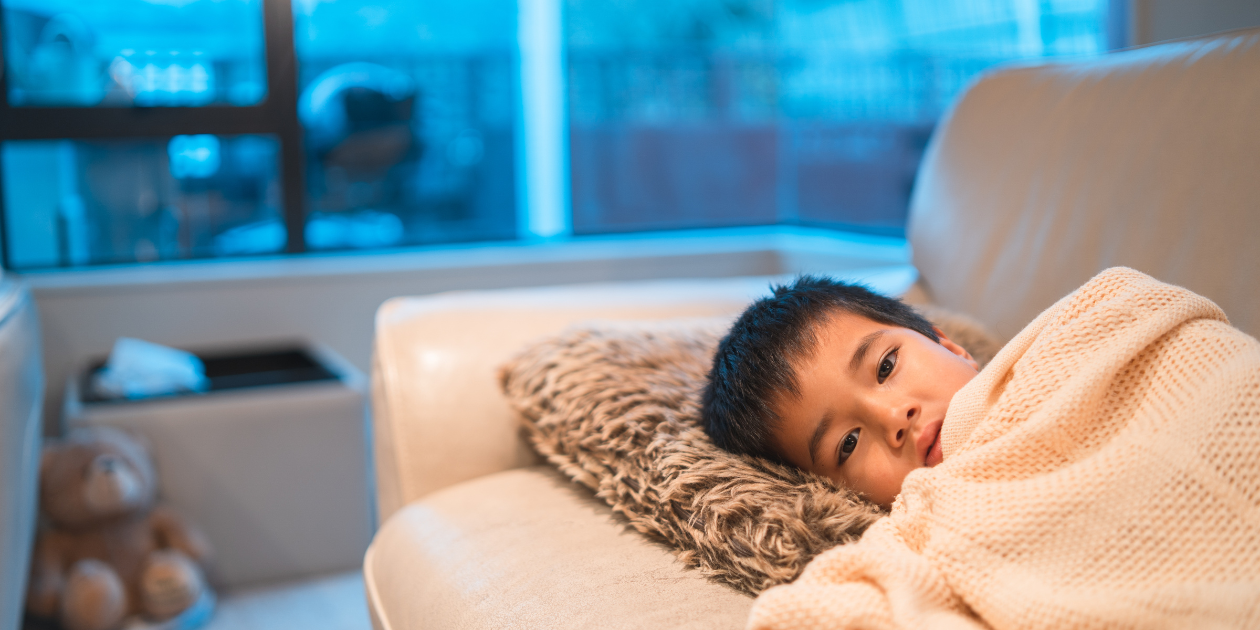 Sick kid laying on a couch with a blanket