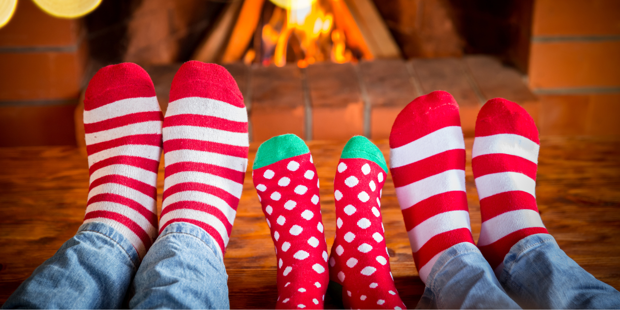 3 pairs of feet wearing red, white and green socks in front of a fire